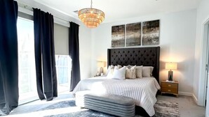 A modern bedroom with a large bed, a tufted headboard, two bedside lamps, and a view of the city through large windows. - Luxe 3Bed Townhome in Heights with WiFi, Private Rooftop, Private Parking (Houston)