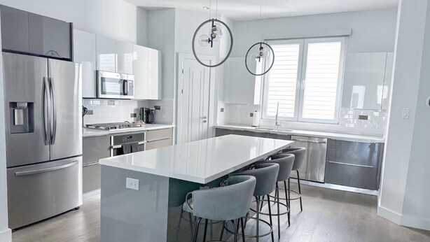 A modern kitchen with stainless steel appliances, a central island with bar stools, and pendant lighting. - Luxe 3Bed Townhome in Heights with WiFi, Private Rooftop, Private Parking (Houston)