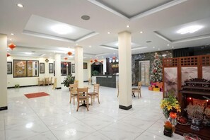 En hotellobby med en receptionsdisk, en sittgrupp och dekorativa element som en julgran och blomsterarrangemang.
