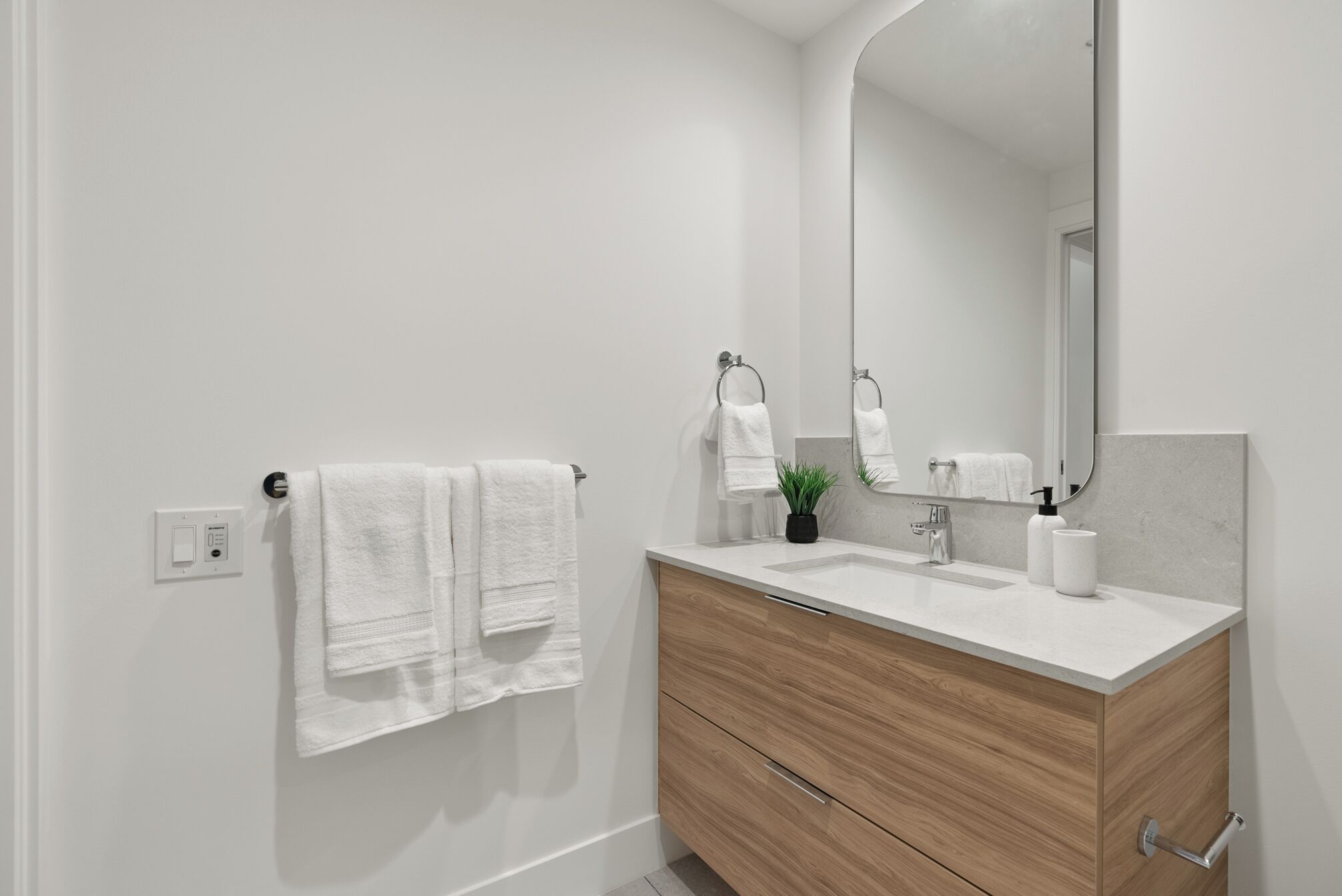 A modern bathroom with a white vanity, a large mirror, and two towels hanging on the wall.