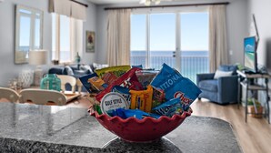 A living room with a large window, a ceiling fan, and a bowl of assorted snacks on a counter. - *Majestic Sun A801*Updated*Heated Pools +Hot Tubs*Gym*Pickleball & Tennis* (Miramar Beach)