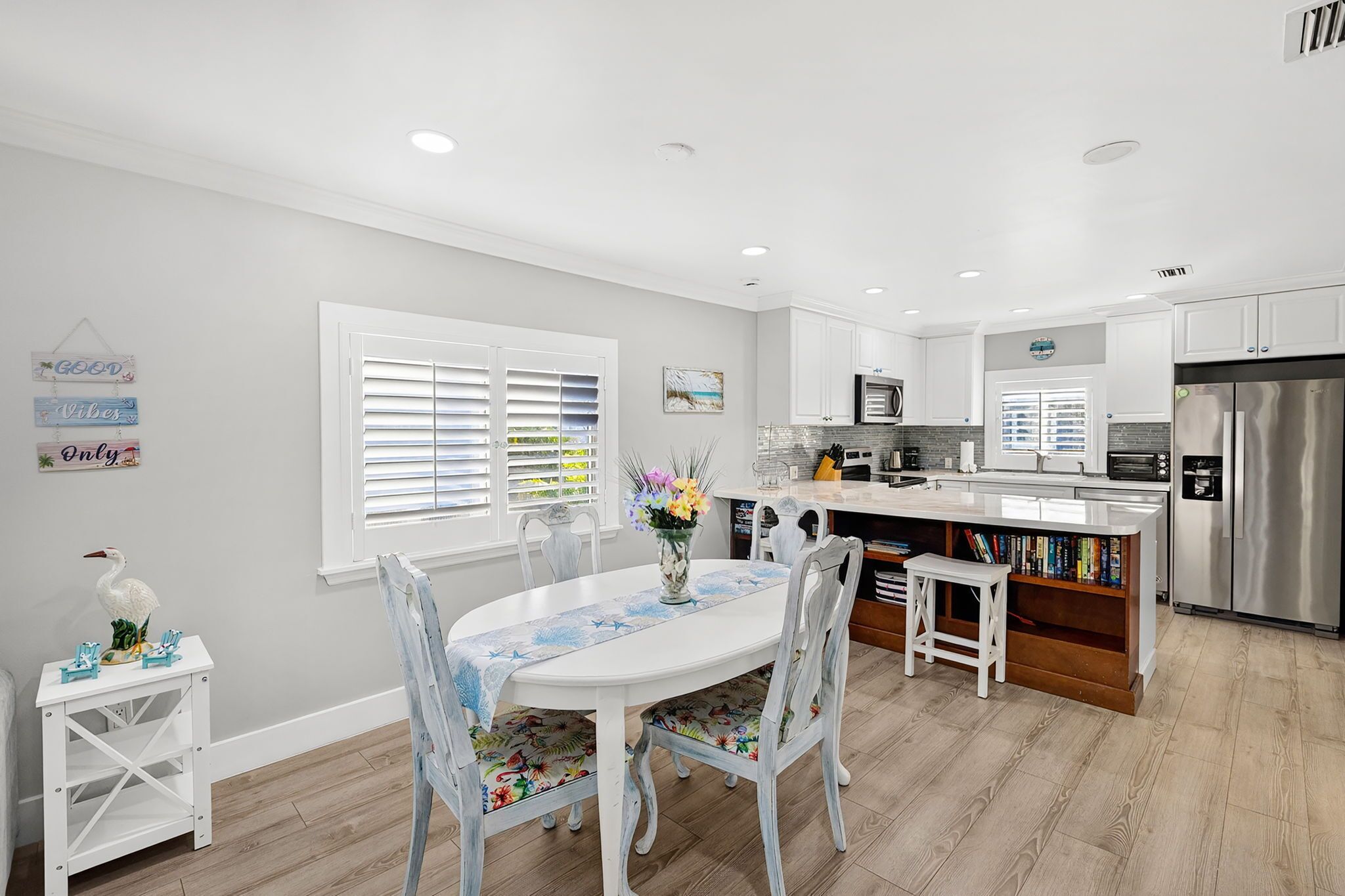 A modern kitchen with white cabinetry, a stainless steel refrigerator, and a dining area with a white table and chairs.