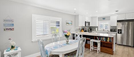 A modern kitchen with white cabinetry, a stainless steel refrigerator, and a dining area with a white table and chairs.