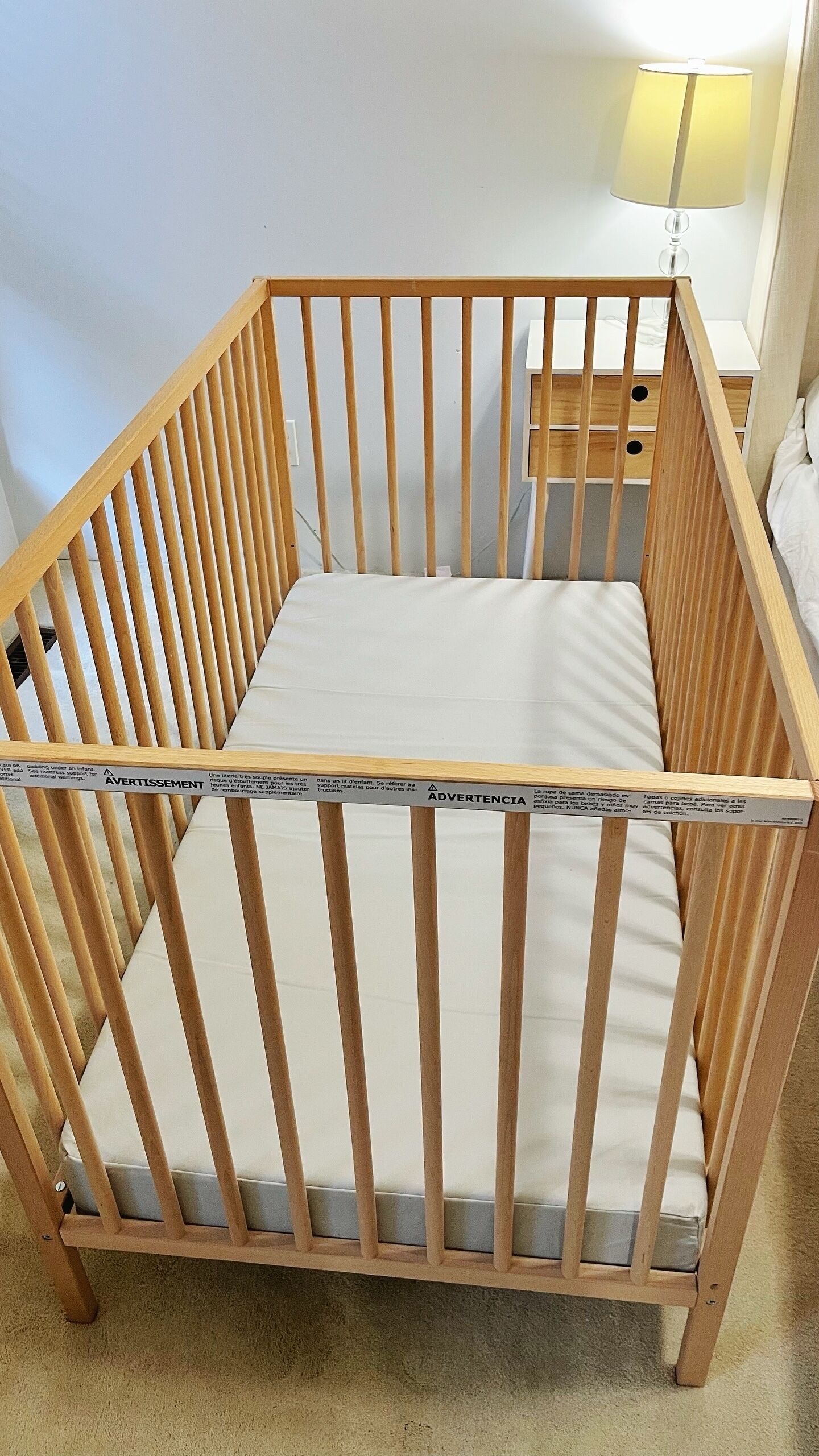 A wooden crib with a mattress and a safety label.