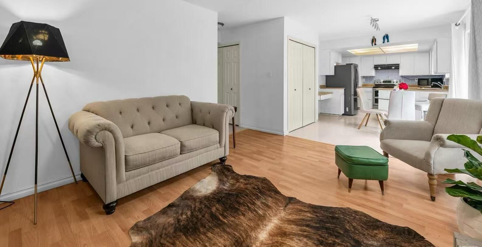 A living room with a beige sofa, a green ottoman, a floor lamp, and a large animal hide rug.