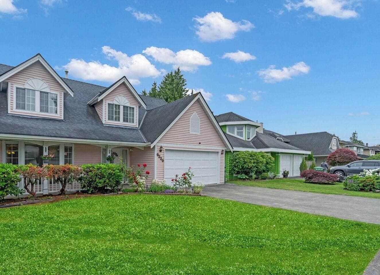 Une maison de banlieue à deux étages, avec un garage à l’avant, une pelouse bien entretenue et un ciel bleu dégagé.