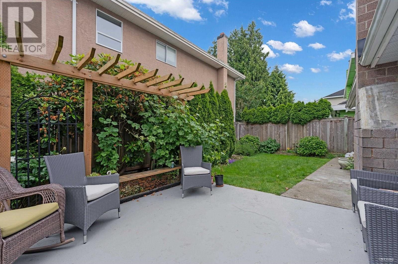 Un patio con mobiliario de mimbre, una pérgola de madera y un jardín con plantas trepadoras.