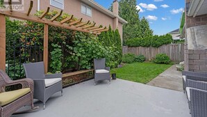 A patio with wicker furniture, a wooden pergola, and a garden with climbing plants.