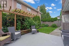 A patio with wicker furniture, a wooden pergola, and a garden with climbing plants.