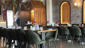 A restaurant with a modern interior, featuring wooden ceiling beams, green chairs, and a bar area with a wooden counter. - The Divine Cloud Inn (Aligarh)