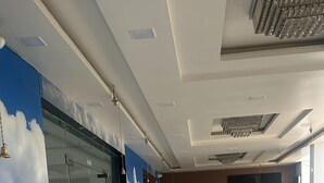 A spacious lobby with a marble floor, a glass wall with a cloud mural, and a reception area with a wooden door. - The Divine Cloud Inn (Aligarh)