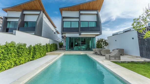 A modern two-story house with a swimming pool in the center, surrounded by a well-maintained lawn and a hedge.