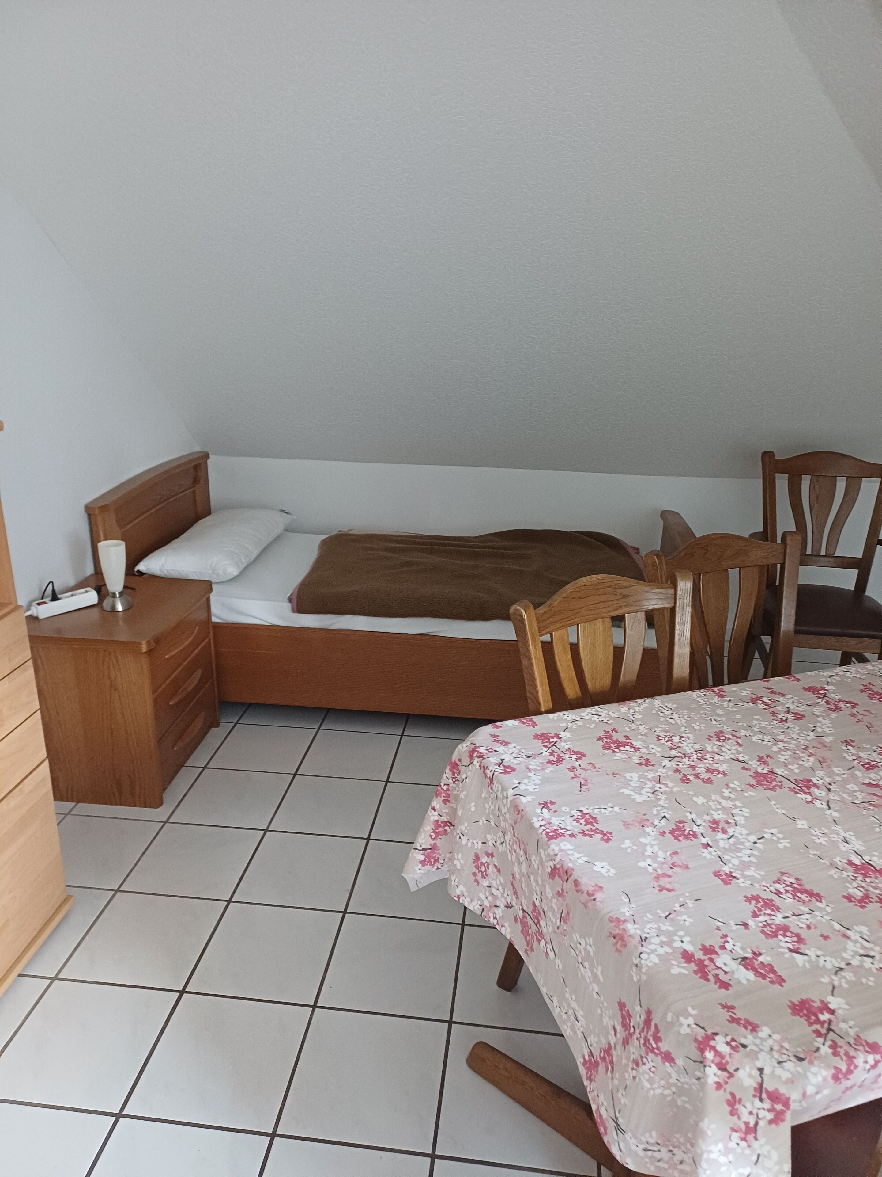Una camera da letto con un letto, un comodino in legno, un tavolino e un tavolo coperto da una tovaglia floreale.