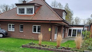 A brick house with a tiled roof, a paved driveway, and a well-maintained garden with various plants and a small tree. - Vacation apartment in Twist, Dutch border, recreational area within walking distance (Twist)