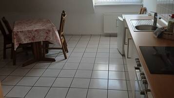 A kitchen with a dining table, chairs, a window with curtains, a radiator, and a sink.