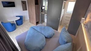 Un intérieur moderne avec un coin salon agrémenté de coussins à motifs bleus, d’une petite table ronde et d’un téléviseur fixé au mur.