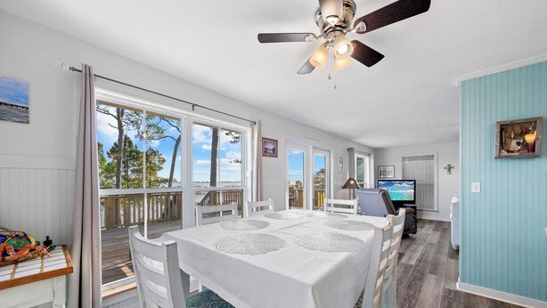 A spacious dining area with a white table set for four, large windows offering a view of the outdoors, and a ceiling fan. - Last Resort (Gulf Shores)