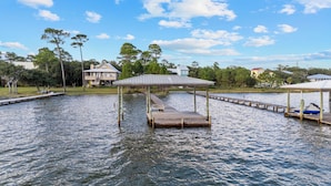 A wooden dock extending into a calm body of water, surrounded by trees and houses. - Last Resort (Gulf Shores)