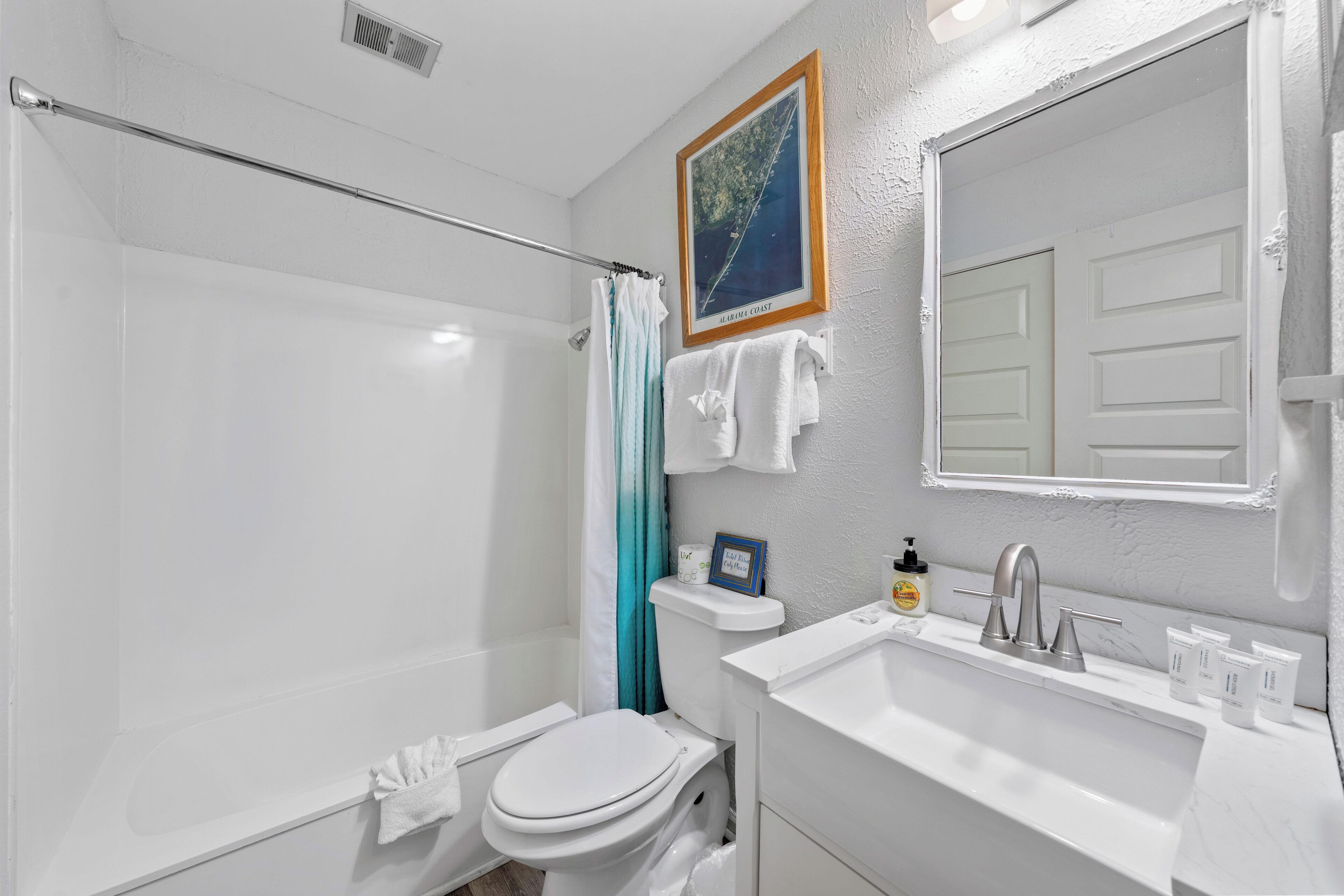 A bathroom with a white toilet, a shower with a glass door, a sink with a mirror, and a framed picture on the wall.