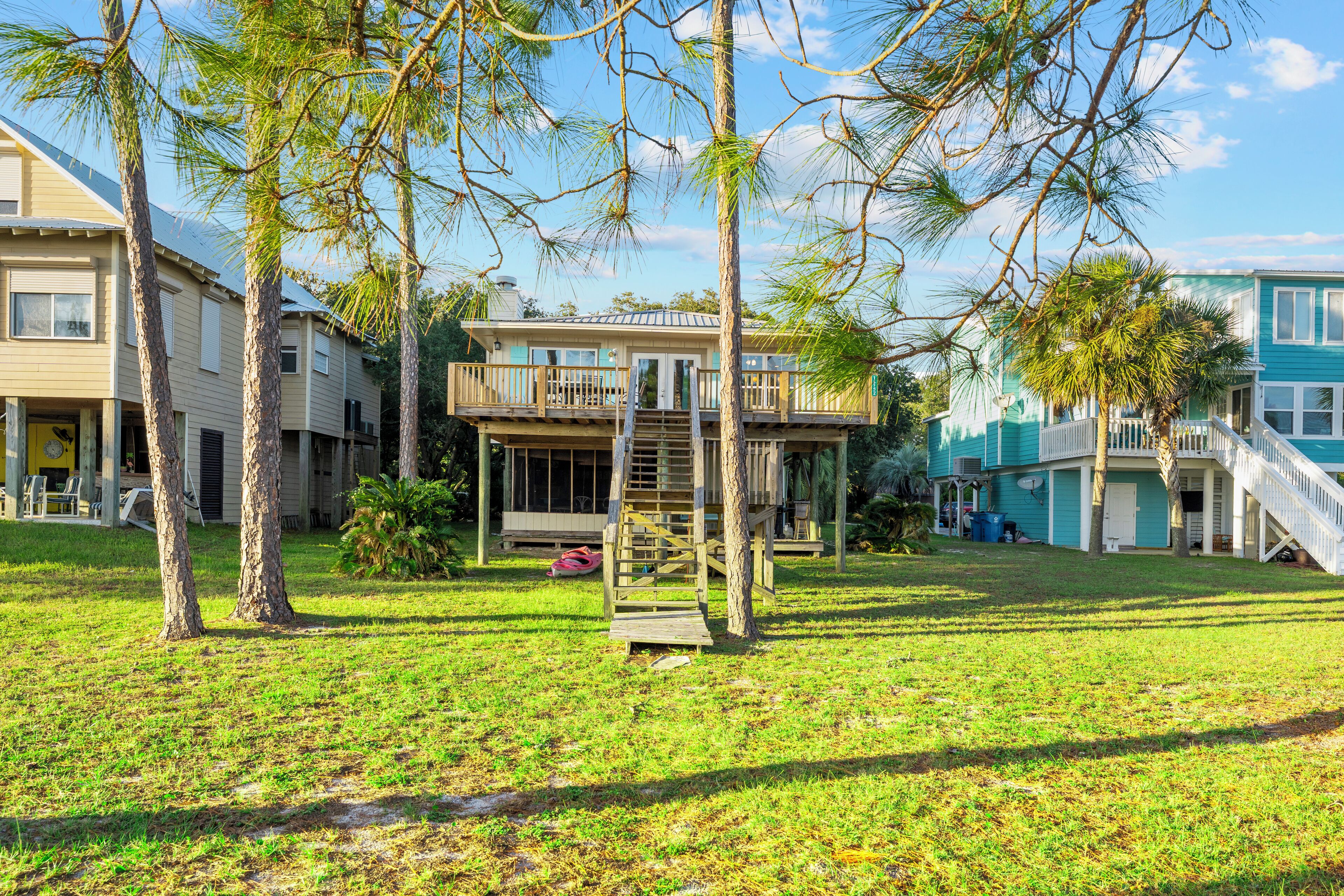 A residential area with a two-story house featuring a balcony, surrounded by trees and a grassy yard.