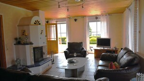 A living room with a fireplace, leather sofa, a TV, and a dining table. - Holiday Home 'Boddenperle' with Sea View, Private Terrace and Wi-Fi (Breege)