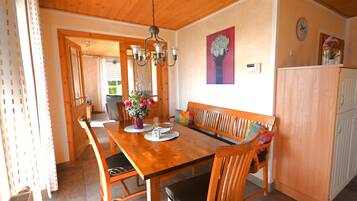 A wooden dining table with chairs, a bench, a vase with flowers, and a clock on the wall.