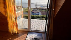 A room with a large sliding glass door leading to an outdoor deck with a view of the sea and boats. - Holiday Home 'Boddenperle' with Sea View, Private Terrace and Wi-Fi (Breege)