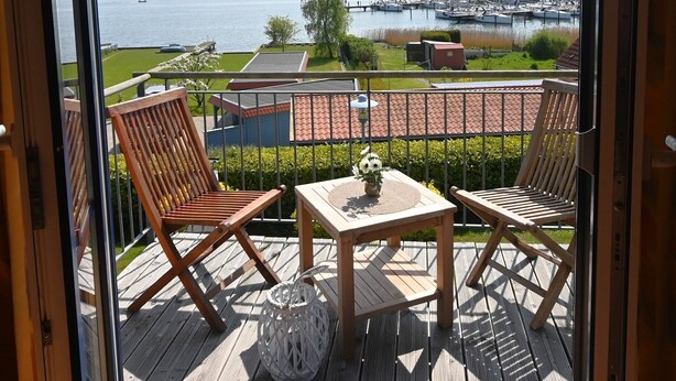 A balcony with wooden furniture, a table with a vase, and a view of a marina with boats. - Holiday Home 'Boddenperle' with Sea View, Private Terrace and Wi-Fi (Breege)