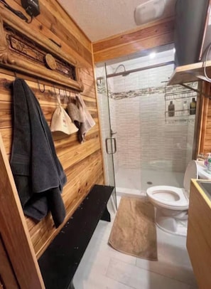 Une salle de bain avec un mur en bois, une douche en verre, des toilettes et un banc.