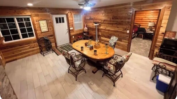 Een gezellige kamer met houten wanden, een ronde eettafel met stoelen, een plafondventilator en een deur.