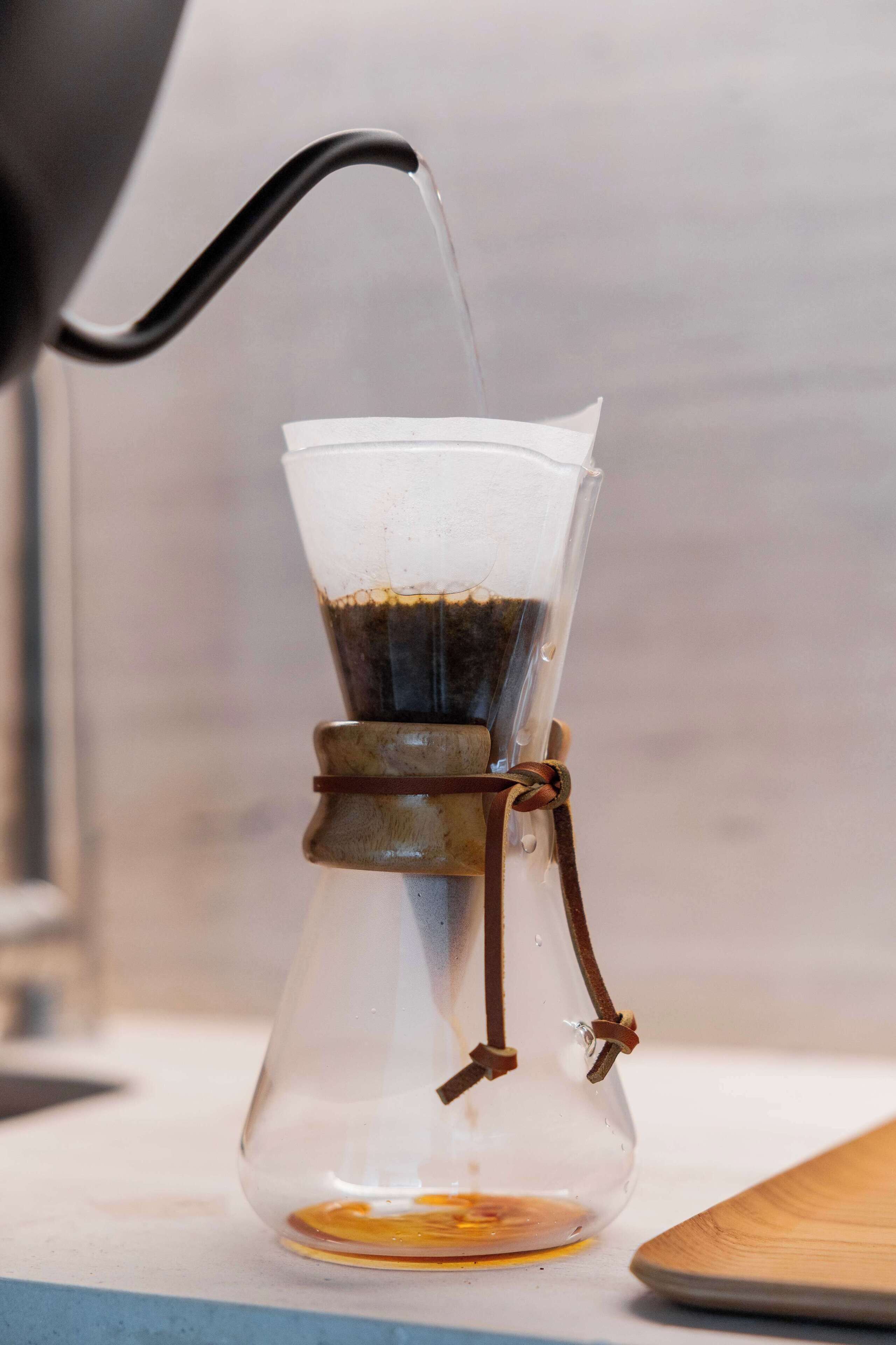 A coffee maker with a clear glass carafe and a metal filter, water is being poured into it.