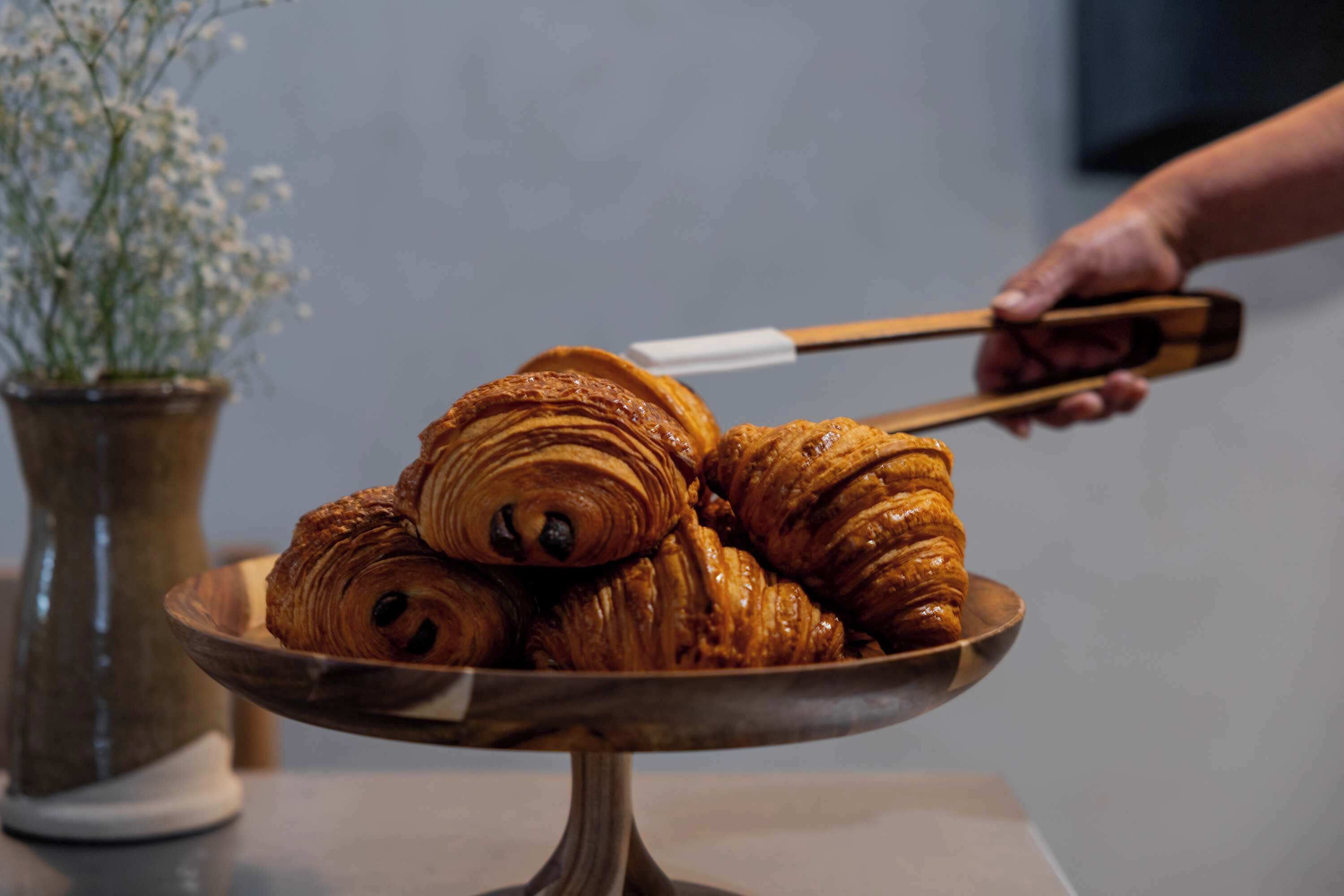 Un piatto di legno porta croissant tenuti da pinze di legno.