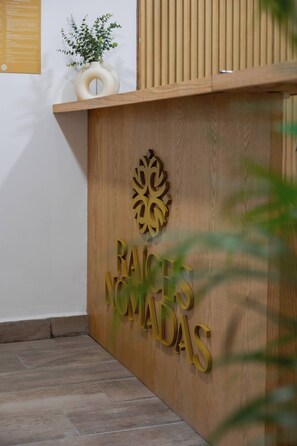 A reception desk with a wooden finish and a logo above the name 'RAICES NOMADAS'.