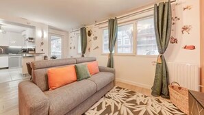 A modern living room with a grey sofa, a patterned rug, and a kitchen in the background. - Starwars Disney 10 minutes by car. Cuisine équipée et Wi-Fi performant (Bussy-Saint-Georges)