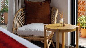 A wicker chair with a white cushion and a brown pillow, a small wooden table with a bottle of reed diffuser, and a view of a balcony with potted plants. - Steps from the Beach at Raíces Nómadas Studio (Puerto Vallarta)