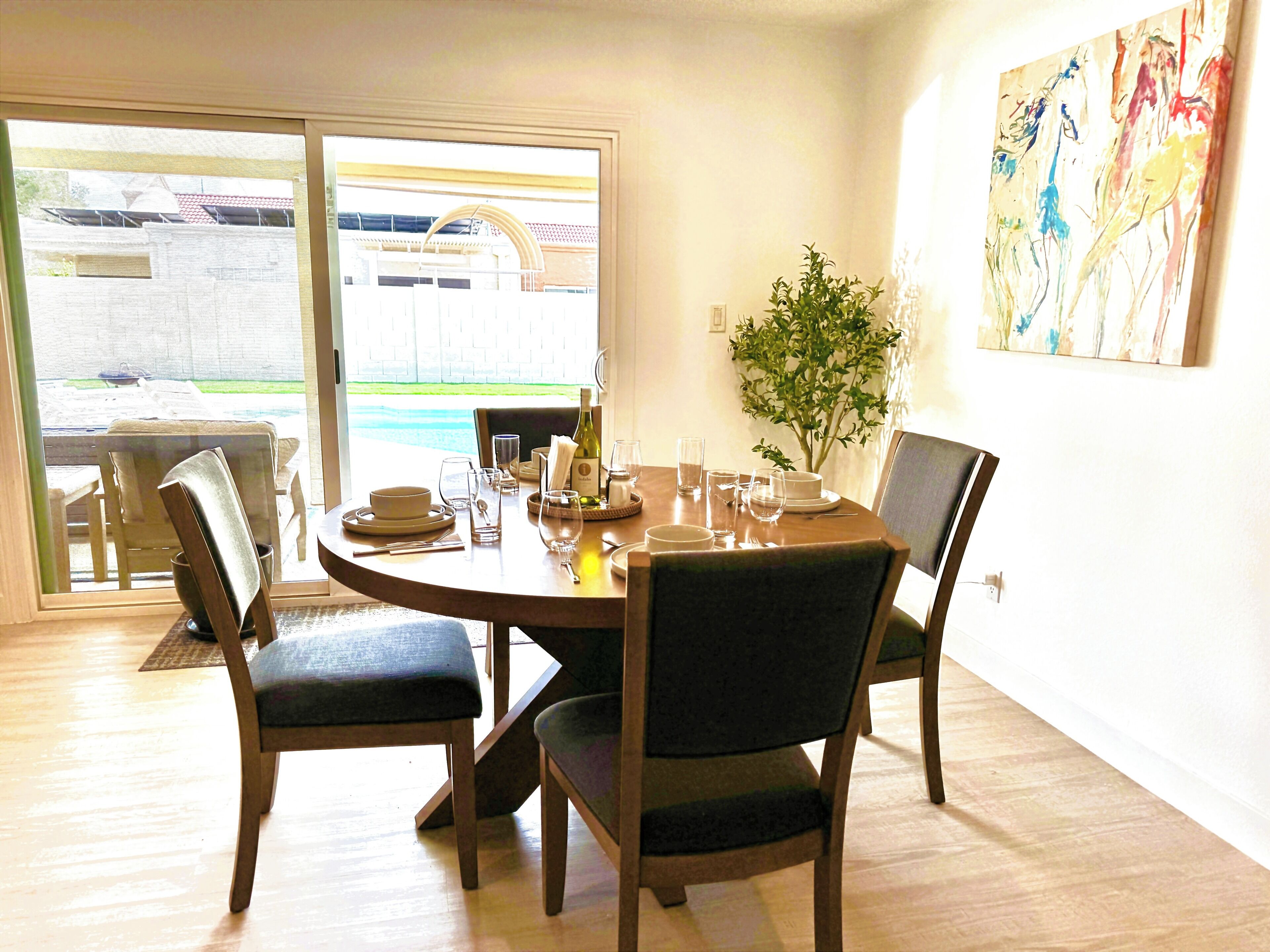 A dining area with a round table set for four, chairs, a vase with greenery, and a painting on the wall.