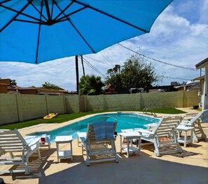 Un patio trasero con piscina, sillas de descanso y una sombrilla.