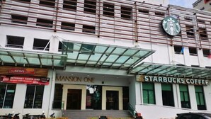 Un bâtiment avec une entrée en verre, une enseigne Starbucks et une autre indiquant « Mansion One ».