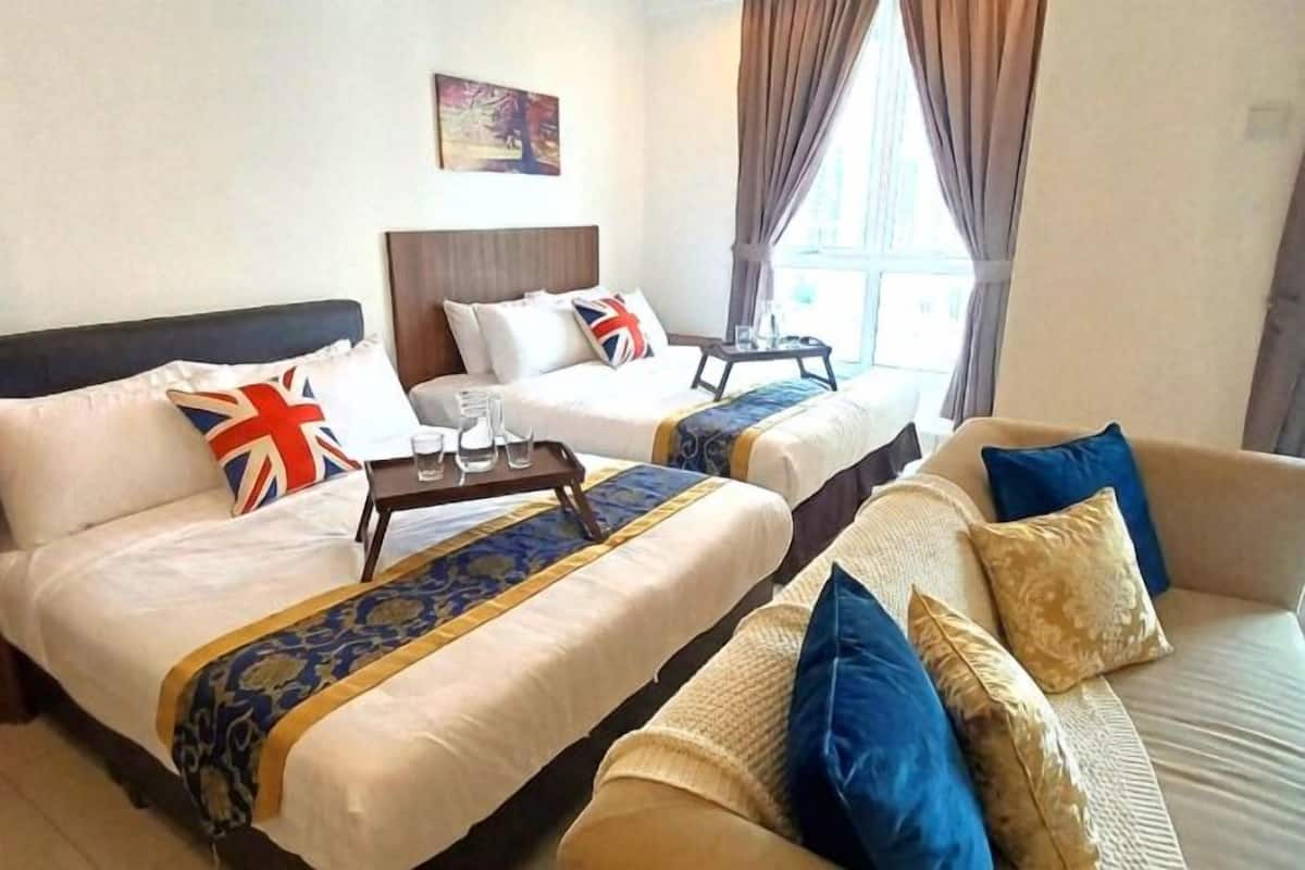 A hotel room with two beds, a sofa, a small table with glasses, and a window with curtains.