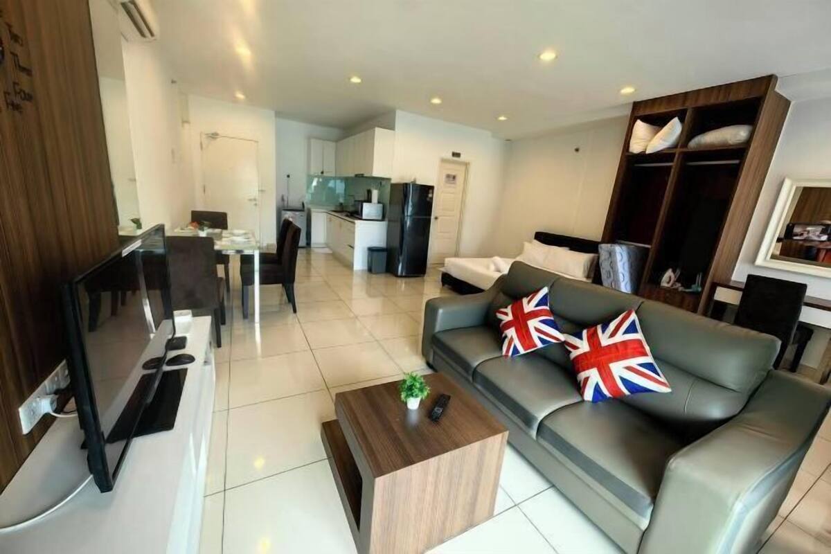 A modern living room with a sofa, a coffee table, a TV, and a kitchen area in the background.