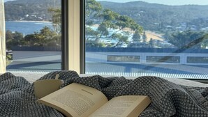 A book on a bed with a view of a coastal landscape through a window.