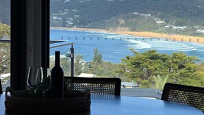 A table with a view of a beach and ocean, a bottle, and wine glasses.