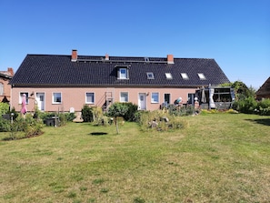 A two-story house with a dark tiled roof, multiple windows, a small garden, and a visible chimney. - Apartment 'Koppelblick' with Private Terrace, Shared Garden and Wi-Fi (Plattenburg)