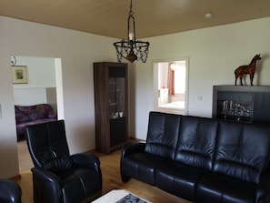 A living room with a black leather sofa, two black leather armchairs, a wooden cabinet with a glass display, and a horse figurine on top.