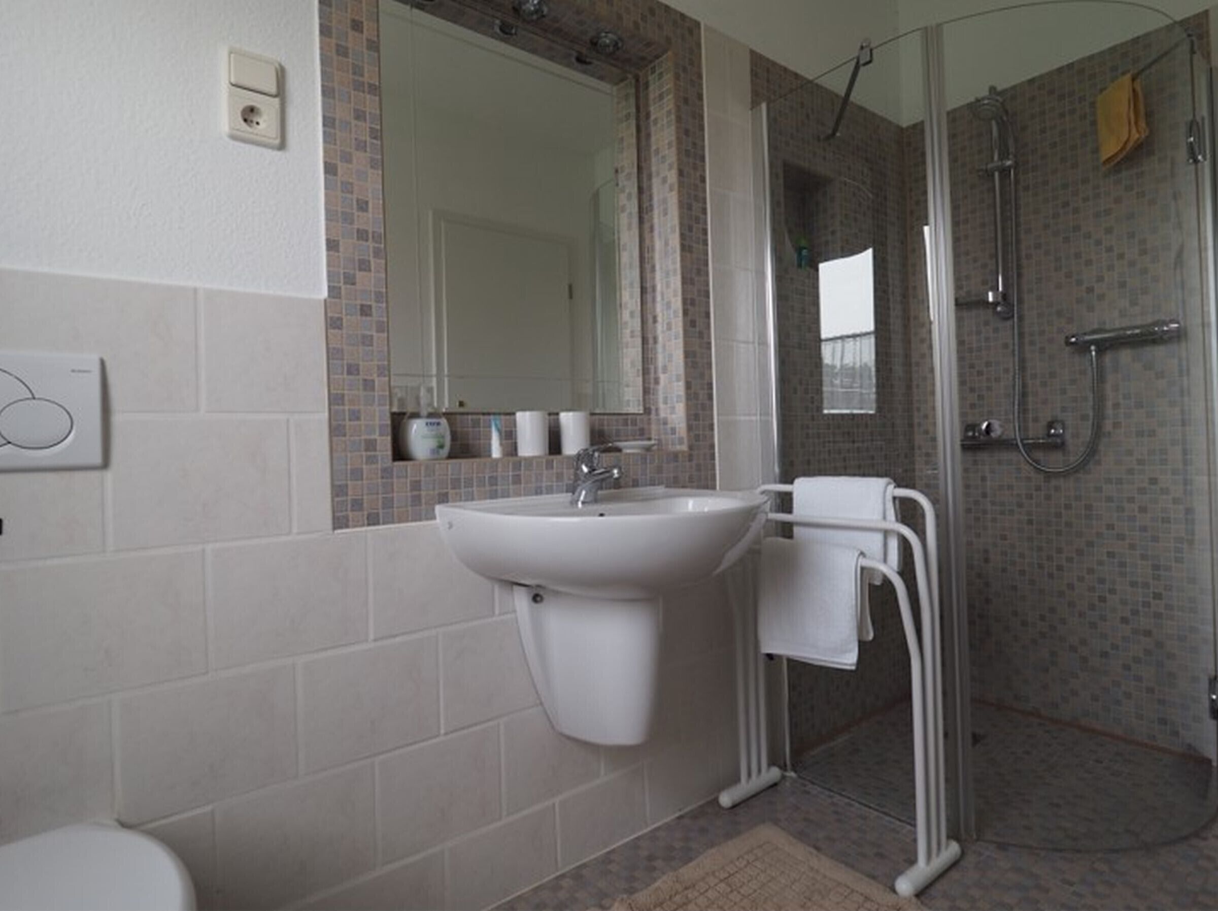 Ein Badezimmer mit einem weißen Waschbecken, einem Spiegel, einer Dusche mit Glastür und einem Handtuchhalter.