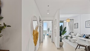 Un salon moderne avec un canapé, une table basse et un coin repas. Un couloir mène à une autre pièce.