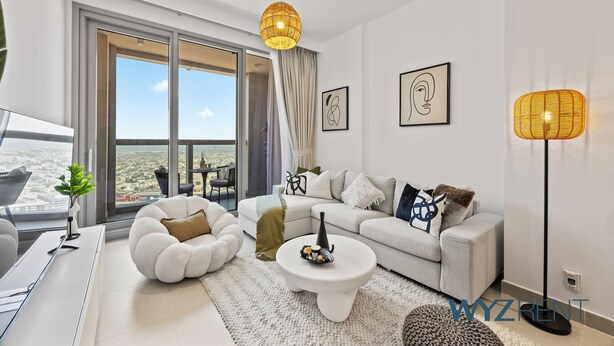 Un salon moderne avec un canapé, une table basse et des coussins décoratifs. Une grande fenêtre offre une vue sur la ville.