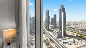 Une vue depuis une fenêtre donnant sur un paysage urbain avec de hauts immeubles, une lampe sur le rebord de la fenêtre et le texte « WYZRENT » dans le coin inférieur droit.