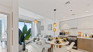 Une cuisine moderne avec des meubles blancs, un coin repas doté d’une table ronde et un salon avec un canapé et une grande plante.