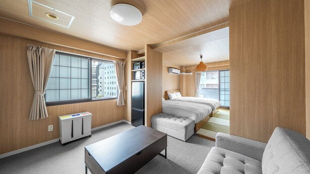 A modern hotel room with a wooden interior, a bed, a sofa, a small table, and a window with curtains. - MITTO (Sapporo)